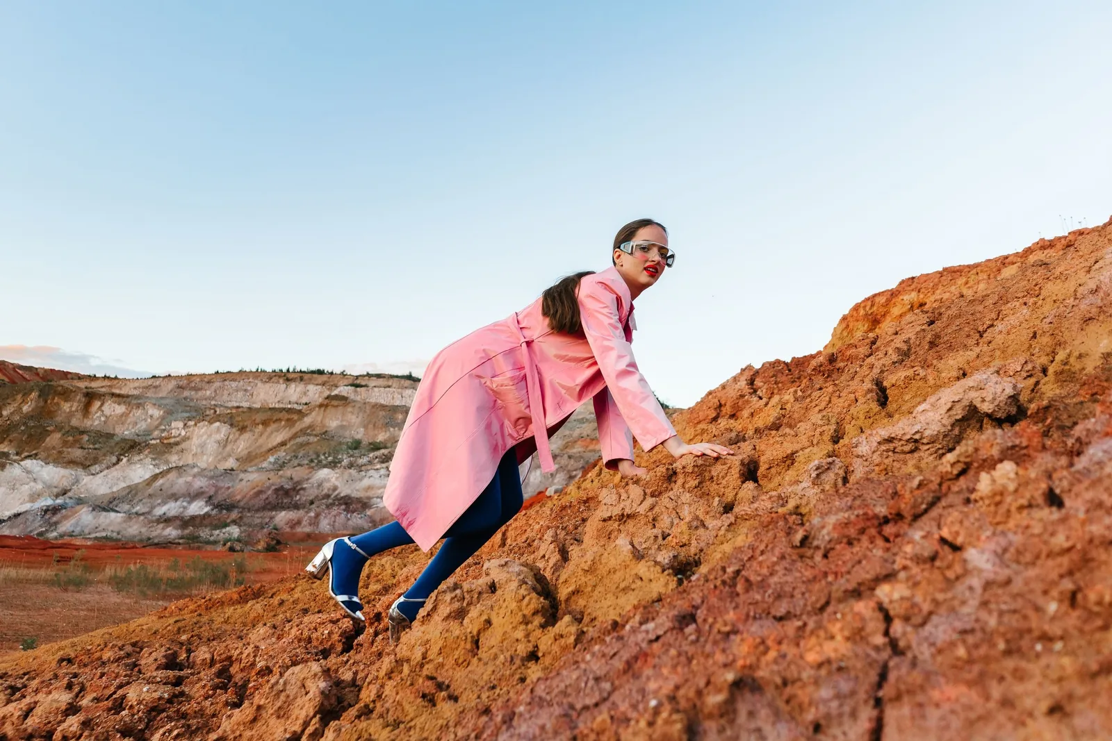 Model climbing a rocky slope in a pink coat